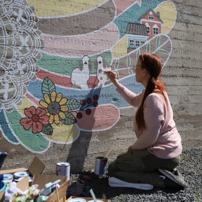 Nainen maalaa värikkäitä siipiä harmaaseen betoniseinään.