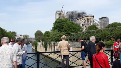 Turister på en bro framför den brandskadade katedralen Notre-Dame 