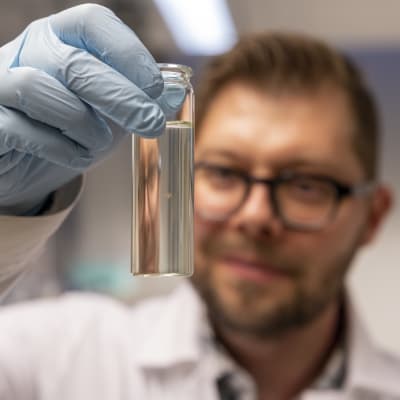 Tutkija Sami Taipale pitelee laboratoriossa käsissään pientä lasipulloa, jossa uiskentelee tutkimuksessa käytetty vesikirppu.