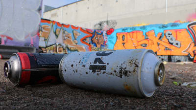 Två tomma sprayfärgsburkar ligger framför en vägg prydd av graffiti. 