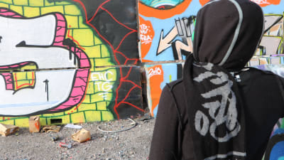En person står framför en vägg målad med graffiti.