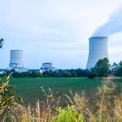 Ett kärnkraftverk med två avsmalnande konkava gråa betongcylindrar reser sig ur terrängen med en central byggnad mellan sig. Ur den ena cylindern stiger det rök, den andra är stilla.