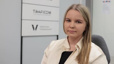 Traficoms jurist Roosa Junttonen sittande. I bakgrunden syns en skylt med Traficoms logo.