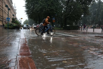 En cyklist leder sin cykel genom en vattenpöl vid ett övergångsställe.
