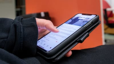 Hand håller i smarttelefon och scrollar med tummen på en sociala medier-app. 