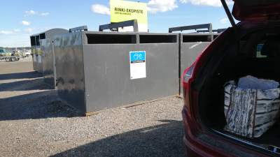 I en baklucka på en bil ser man kasse med sorterat avfall som ska lämnas i behållarna i bakgrunden.
