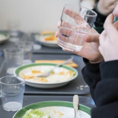 Delvis uppätna skolmatsportioner på brickor. En hand håller i ett vattenglas.