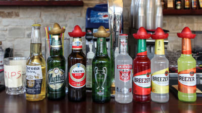Åtta flaskor med olika alkoholdrycker står uppradade på en bardisk.