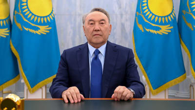 Kazakstans tidigare president Nursultan Nazarbajev vid ett bord, i bakgrunden kazakiska flaggor.