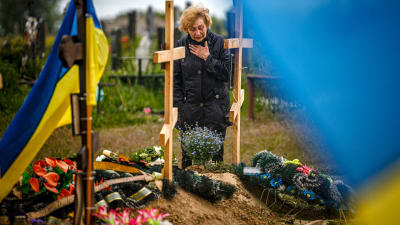En kvinna står framför en rad gravar. Bredvid gravarna vajar Ukrainas flagga.