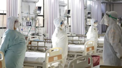 sjukvårdare i skyddsutrustning står bredvid sängar i ett sjukhus