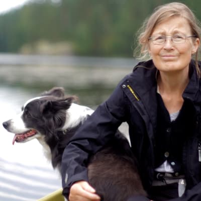 En äldre kvinna sitter i en båt med en bordercolliehund.