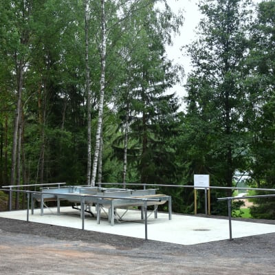 Modern mattvätt på betongplatta invid skog med badstrand i bakgrunden.