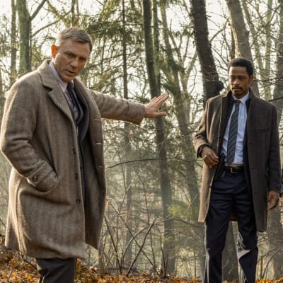 Benoit Blanc (Daniel Craig) står i skogen tillsammans med poliserna Elliott (LaKeith Stanfield) och Trooper Wagner (Noah Segan) och försöker kolla fotspår i leran.