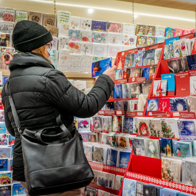 Nainen katselee joulukortteja kirjakaupassa hengityssuojain kasvoillaan.