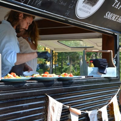 Patrik Laine serverar mat ur serveringsluckan på sin foodtruck medan en kund står bredvid och väntar.