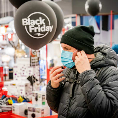 En person i ansiktsmask vid ingången till en butik under Black Friday.
