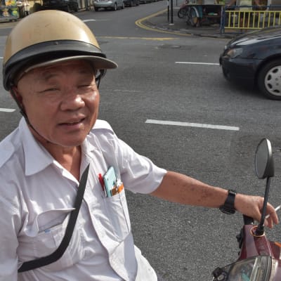 Lee Tion Lai sitter på en moped, med en cigarett i handen.
