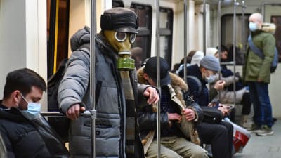 Människor på metron i Moskva. En man bär en gasmask, de andra munskydd.