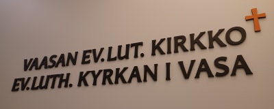 Skylt med texten Vaasan ev.lut. kirkko/Ev.luth. kyrkan i Vasa och ett litet kors till höger
