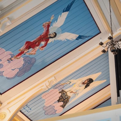 Kaksi kirkasväristä enkeliä maalattuna kirkon kattoon, yksi kiinalaisen naisen näköiseksi, toinen romaninaisen näköiseksi.