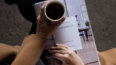 En kvinna sitter med ett köpebrev och en kaffe i famnen.