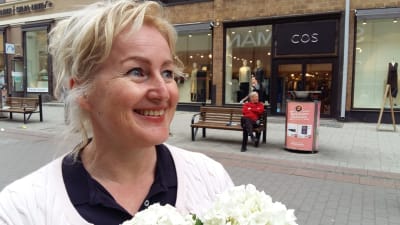 Helena Särkijärvi, en dam med ljust hår, vit tröja och vita blommor i famnen.