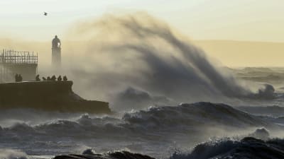 Bild på människor som står på en pir som omges av höga vågor.