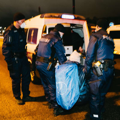 Kaksi poliisia kantaa mielenosoittajaa poliisiautoon. Kolmas poliisi seuraa vierestä.