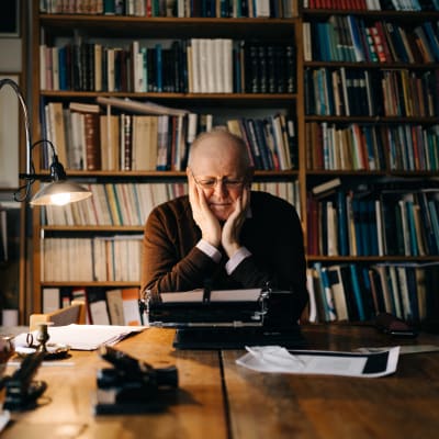 Kirjailija Antti Tuuri istuu työhuoneellaan kirjoituskoneen äärellä ja nojaa käsiinsä.