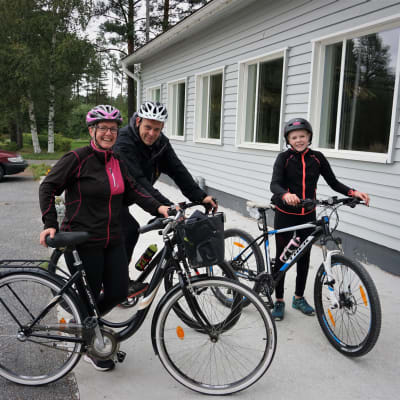 En familj på cykel står framför en vit byggnad.