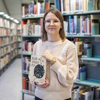 Camilla Nissinen seisoo kirjastossa Rihmasto-teos käsissään.