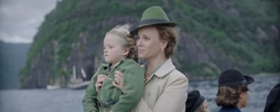 En liten trasnportbåt. Ombord ser vi Märtha som håller i sonen Harald och de tittar båda framåt.