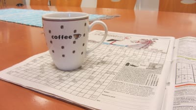 Ett korsord och en kaffekopp på ett köksbord.