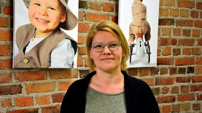 Virpi Hagström står framför en tegelvägg prydd av tavlor med fotografier av barn.