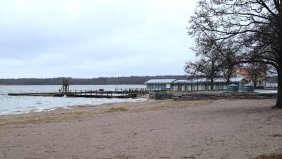 En tom strand. I bakgrunden skymtar en siminrättning.