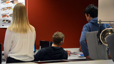 Tre ungdomar sitter med ryggen mot kameran vid en dator i en skola