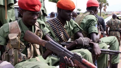 Sittande soldater i gröna uniformer, röda mössor och vapen.