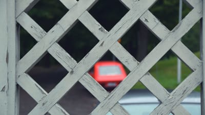 Sliten målarfärg på staket, i bakgrunden en gammal röd bil.