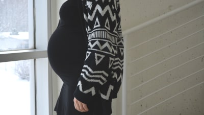 Gravid kvinna står vänd i profil mot kameran vid ett fönster