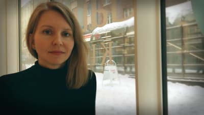 Nora Hämäläinen tittar in i kameran, genom fönstret bakom ser man en snöig gatubild.