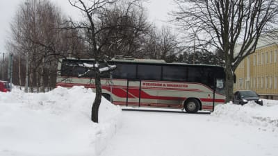 En grå och röd buss åker nerför en snöig gata.