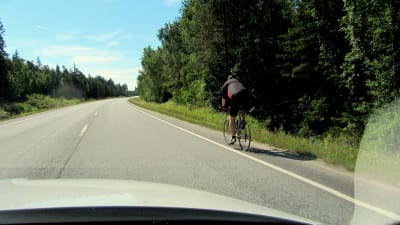 En landsvägscyklist blir omkörd av en personbil.