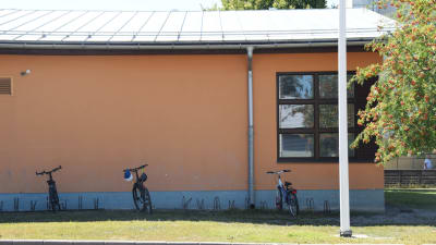 En bild på ett hus. Framför huset står tre cyklar i en cykelställning och brevid huset växer rönnbär.