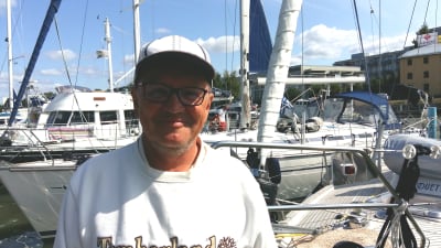 Martti kautto, en man med vit skärmmössa och vit tröja står i en gästhamn bland båtar.