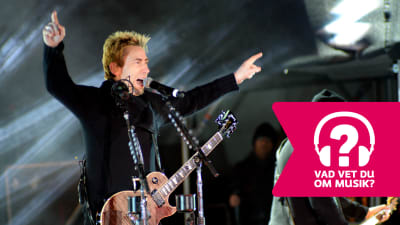 Chad Kroeger står med uppsträckta händer, har en elgitarr kring halsen och sjunger i en mikrofon.