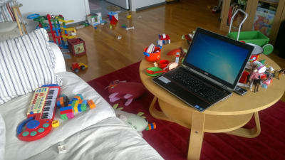 Laptop i vardagsrum fyllt av leksaker.