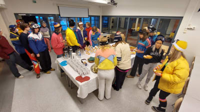 Ungdomar i skidkläder, mössa och skidglasögon inne i Virkby skola där de plockar åt sig frukostmat. Penkis i Virkby.