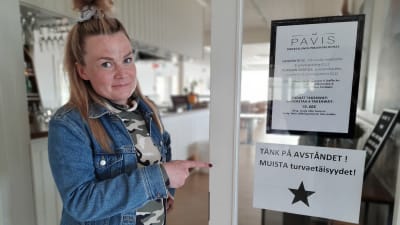 Emma Sandström-Sunqvist, krögare på Pavis pekar på en skylt om säkerhetsavstånd under coronatider. 