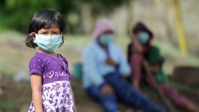 En liten flicka och hennes familj bär ansiktsmasker då de arbetar på sin odling i Kubu, Bali. 27.11.2017.
